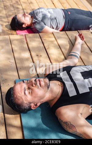 Von oben der friedlichen jungen ethnischen tätowiert Männchen nachbilden mit Geschlossene Augen in der Savasana-Pose nach dem Yoga-Unterricht im Freien Stockfoto