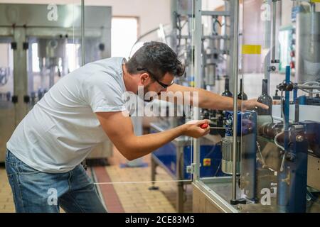 Seitenansicht konzentrierte bärtige männliche Winzer in Freizeitkleidung arbeiten Mit professioneller Weinkellerei Ausrüstung in der Fabrik Stockfoto