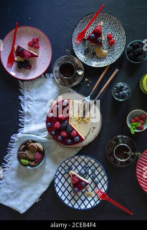 Von oben leckeren Kuchen mit Marmelade Belag auf Holz gelegt Tablett neben verschiedenen Beeren serviert auf dem Tisch auf schwarzem Hintergrund Stockfoto