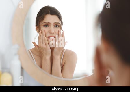Gestresstes Mädchen berührt ihre Haut und Blick auf Spiegel Stockfoto