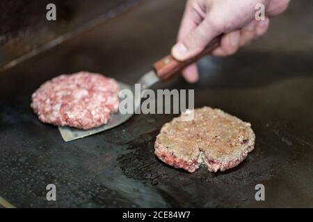 Unkenntlich Koch bereitet Koteletts aus Hackfleisch für Burger während Stehen am Herd mit Spachtel Stockfoto