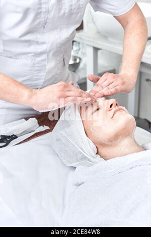 Männliche Kosmetikerin spendet Feuchtigkeit und reinigt sein Gesicht mit Sahne Seife. Frau in der Spa-Behandlungen Stockfoto