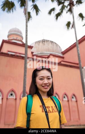 Asiatische weibliche Reisende in Bogenfenster der Pink Mosque stehen Während Sightseeing in Kota Kinabalu während der Sommerferien und suchen Bei der Kamera Stockfoto