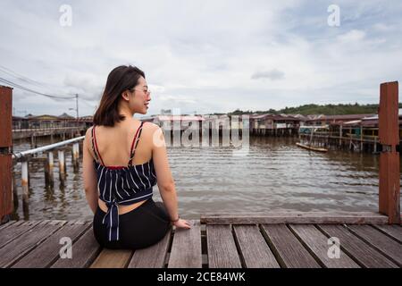 Rückansicht der entzückten ethnischen weiblichen Touristen entspannen am Kai In Kampong Ayer schwimmenden Dorf und wegschauen beim Genießen Urlaub in Bandar Seri Begawan Stockfoto
