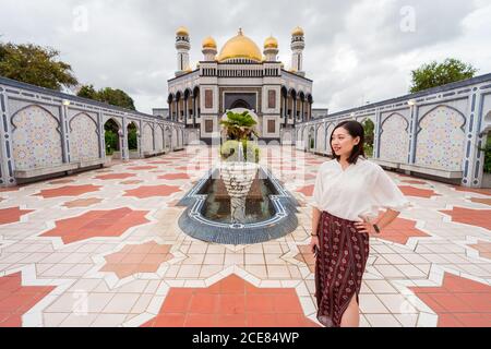 Lächelnde ethnische Reisende auf dem Platz in der Nähe von Jame ASR Hassanil Bolkiah Moschee während Sommerferien in Brunei und suchen Weg Stockfoto