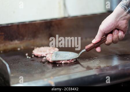 Unkenntlich Koch bereitet Koteletts aus Hackfleisch für Burger während Stehen am Herd mit Spachtel Stockfoto