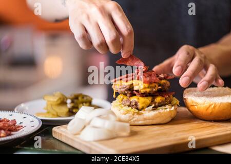 Männlicher Koch steht am Tisch und fügt Fleisch auf schmackhaft Burger-Cutlet Stockfoto