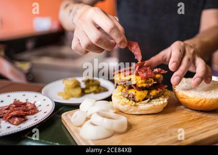 Männlicher Koch steht am Tisch und fügt Fleisch auf schmackhaft Burger-Cutlet Stockfoto