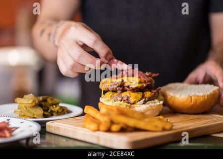 Männlicher Koch steht am Tisch und fügt Fleisch auf schmackhaft Burger-Cutlet Stockfoto