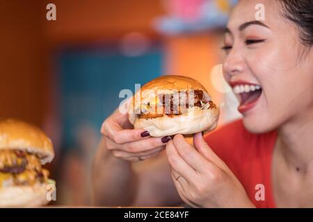 Crop ethnischen weiblich genießen köstliche Burger mit Rindfleisch Cutlet und Sauce im Café Stockfoto