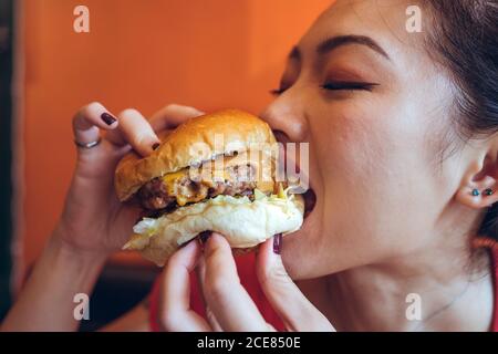 Crop ethnischen weiblich genießen köstliche Burger mit Rindfleisch Cutlet und Sauce im Café Stockfoto