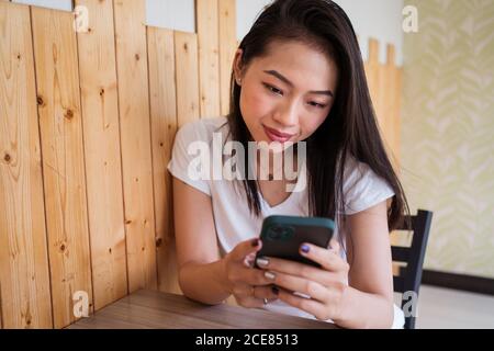 Glückliche Frau, die einen Mann auswählt, während sie sich im Restaurant ausruhte und die Dating-App auf dem Smartphone durchstöberte Stockfoto