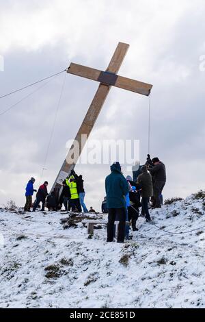 Menschen (Christen) verwenden Seile, um ein riesiges schweres hölzernes Osterkreuz (Faith Symbol) auf einem verschneiten Hügel zu heben - der Chevin, Otley, Yorkshire, Großbritannien. Stockfoto