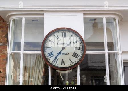 Eine alte hölzerne Uhr an der Außenseite eines Erkerfensters in einer Hauptstraße, Hambledon, Hampshire Stockfoto