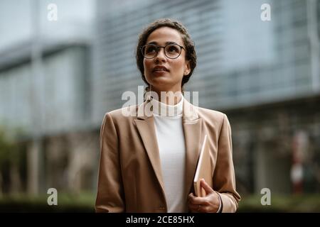 Geschäftsfrau mit Laptop im Freien. Frau in formalwear und Brillen zu Fuß in der Stadt. Stockfoto