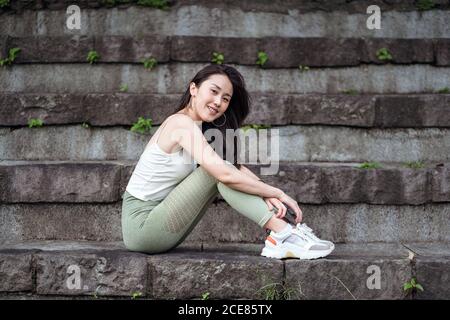 Positive ethnische Frau, die auf schäbigen Treppen im Park sitzt Stockfoto