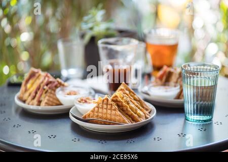 Köstliche Sandwiches auf dem Teller und erfrischende Getränke in Gläsern platziert Auf dem Tisch auf der Sommerterrasse des Cafés Stockfoto