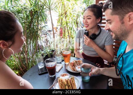 Gesellschaft von verschiedenen Freunden, die sich am Tisch im Sommercafé treffen Und genießen Sie leckere Getränke und Desserts Stockfoto