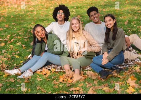 Junge unbeschwerte Freunde sitzen auf dem Boden im öffentlichen Park Stockfoto