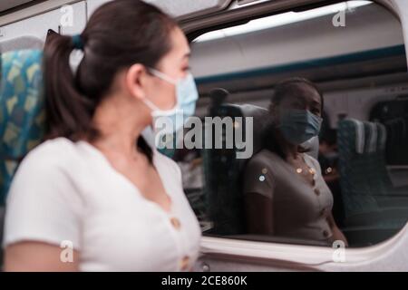 Defokussierten jungen asiatischen Frau in Gesichtsmaske sitzen in der Zugkabine und Blick auf Reflexion auf das Fenster während der Nacht Reise Stockfoto
