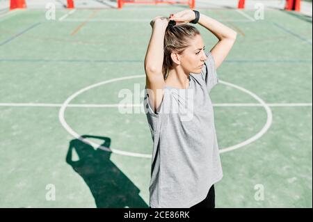 Crop von jungen fit weiblich in Sportbekleidung Anpassung Haar während Vorbereitung auf das Training auf dem Platz Basketball in sonnigen Sommertag Stockfoto
