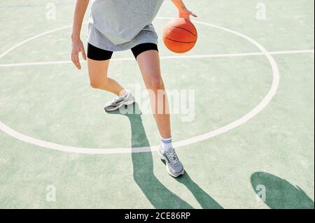 Crop anonyme sportliche Frau üben Dribbling mit Basketball-Ball während Allein spielen auf dem Sportplatz in sonnigen Tag Stockfoto