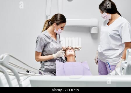 Frauen in medizinischen Uniform und Maske im Gespräch mit weiblichen Patienten Vor Beginn des Heilverfahrens in der Zahnarztpraxis Stockfoto