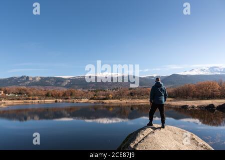 Rückansicht des männlichen Forschers in warmer Kleidung, auf dem steht Felsen am See und bewundern spektakuläre Berglandschaft Stockfoto