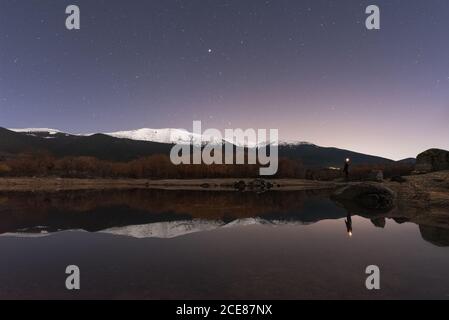 Rückansicht von nicht erkennbaren entfernten Wanderer in der Nähe von See und stehen Genießen Sie spektakuläre Landschaft von Schneebergen mit dunklem Himmel und Sterne in Frühlingsnacht Stockfoto