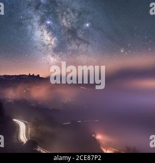 Sternenhimmel mit Milchstraße über nebliger Berglandschaft mit Kurvenreiche Straße vor Sonnenaufgang Stockfoto