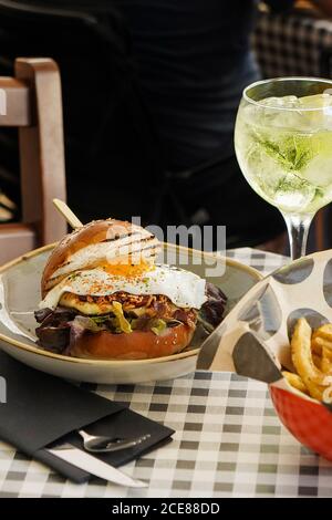 Köstliche Mahlzeit von saftigen Burger mit Spiegelei und Pommes frites Auf dem Tisch mit einem Glas kühlem Limettencocktail im Café Stockfoto