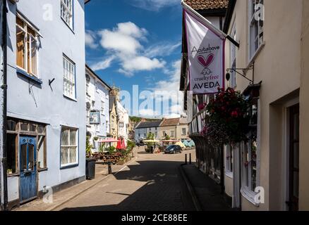 Die Sonne scheint auf traditionellen Geschäften, Pubs und Häusern der High Street und des Marktplatzes in Axbridge, Somerset. Stockfoto