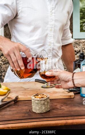 Gesichtsloser Barkeeper, der Kristalldekanter hält und Bourbon eingießt Glas eines männlichen Gastes über der Theke auf der Veranda des Cafés Stockfoto