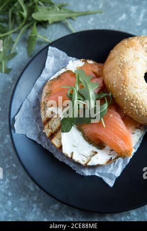 Blick von oben auf appetitliche italienische Bruschetta mit gegrilltem Brotlaib Bedeckt mit Weichkäse und gesalzenem rotem Fisch mit frischem Rucola Blätter auf der Oberseite in der Nähe weich gebackenen Bagel Stockfoto