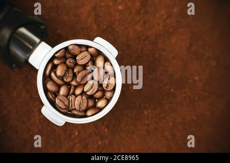 Im Halter der Kaffeemaschine sind geröstete aromatische Kaffeebohnen, und der Halter ist auf dem Hintergrund des gemahlenen Kaffees. Bald werden die Kaffeebohnen zwil Stockfoto