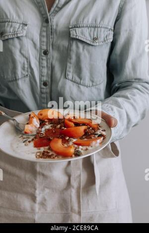 Nicht erkennbare Person in Schürze stehend mit Schale von gesunden Granola Mit Joghurt und frischem Obst Stockfoto