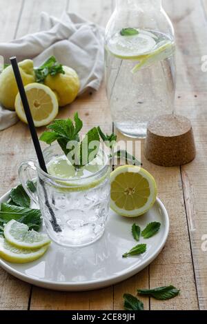 Kaltes Erfrischungsgetränk mit Sodawasser und Zitrone garniert mit Frische Minzblätter auf Glasbecher mit Stroh serviert Holztisch Stockfoto