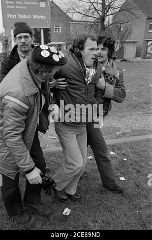 Einem verletzten Bergmann wird während des Bergarbeiterstreiks von 1984 von anderen Streikposten in Port Talbot Steelworks, Südwales, geholfen Stockfoto