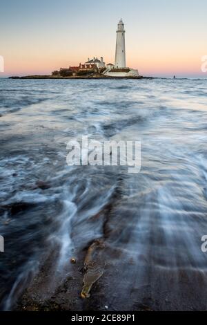 Wellen, Strömung gegenüber der St. Maria Island Causeway in der Dämmerung, mit St Mary's Leuchtturm hinter, auf der Whitley Bay Küste von Tyneside. Stockfoto