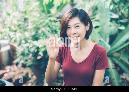 Schönes Porträt junge asiatische Frau lächelnd winkende Hand im Garten zu Hause, freundliches Mädchen und Ausdruck positive Emotion, Hallo und Gruß, ein Stockfoto