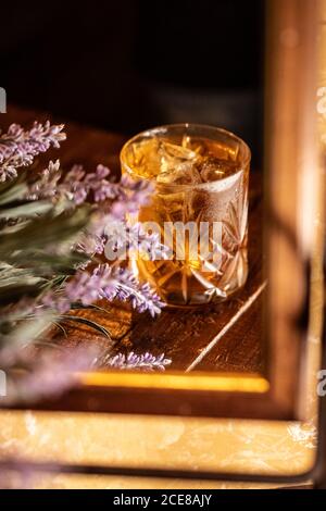 Altmodisches Glas mit Alkoholgetränk auf den Tisch gestellt mit Lavendel blüht und spiegelt sich im Spiegel Stockfoto