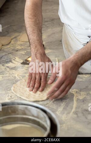 Crop gesichtslosen italienischen männlichen Chef in weißen Uniform Abflachung und Stretching Pizzateig auf Marmor Oberfläche in Pizzeria Küche Stockfoto