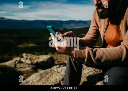 Cropped nicht erkennbar bärtigen Mann Browsing Smartphone während der Ruhe in Puerto De la Morcuera Berge gegen bewölkten Himmel in Spanien Stockfoto