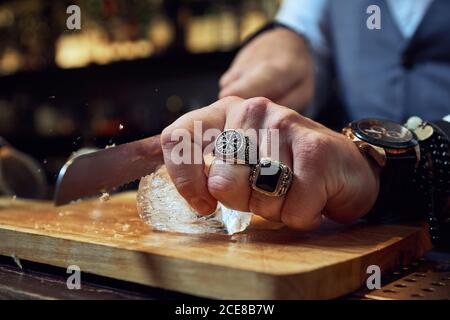 Cropped unkenntlich professionelle Barkeeper Schneiden Eiswürfel mit Messer auf Holzbrett während der Zubereitung eines Cocktails in der Bar Stockfoto