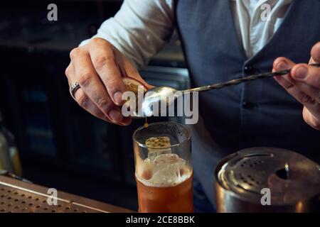 Cropped unkenntlich professionellen Barkeeper hinzufügen Passionsfrucht mit Löffel in Ein frischer Cocktail während der Zubereitung in der Bar Stockfoto