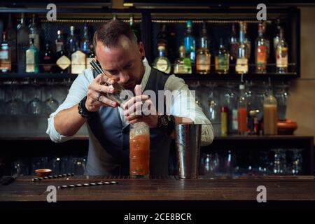 Bärtiger professioneller Barkeeper gießt Eiswürfel in einen Cocktail hinein Ein Glas bei der Arbeit in einer Bar Stockfoto