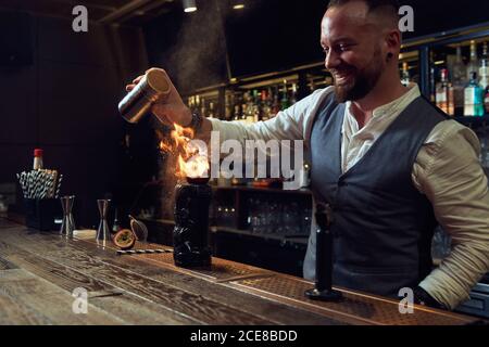 Professioneller junger Barkeeper, der einen Cocktail mit Salz und Feuer verbrennt Mit Glas in der Flamme in der Bar Stockfoto