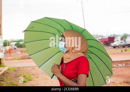 Junge schöne Frau in Hijab trägt einen Regenschirm und trägt Eine medizinische Maske Stockfoto