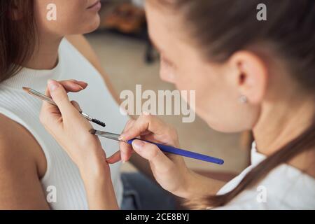 Crop konzentrierte Make-up Künstler Anwendung schwarzen Eyeliner auf junge schön Weibliche Client Augenlider während der Arbeit in zeitgenössischen Studio Stockfoto