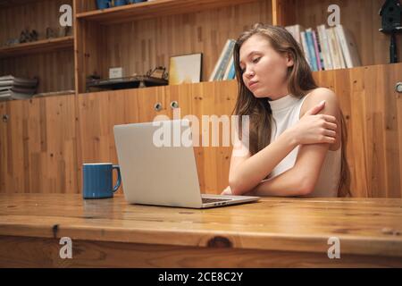 Niedriger Winkel der seriösen jungen ethnischen weiblichen Freiberufler sitzen an Holztisch mit Laptop während der Arbeit aus der Ferne in der modernen Bibliothek Stockfoto